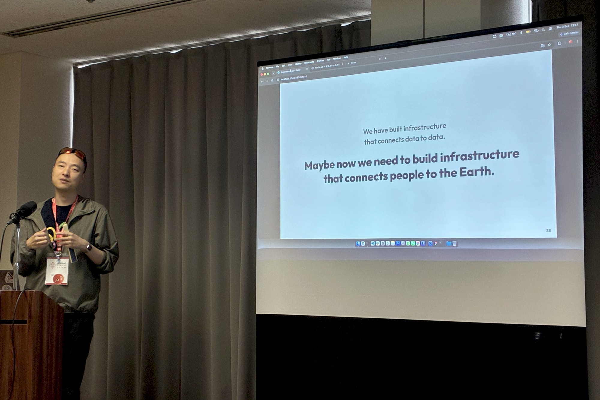 FOSS4G 2026 広島・讲台上,屏幕上是「connects people to the Earth」